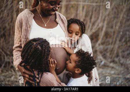 Mère enceinte noire et enfants de course mélangés embrassant le ventre Banque D'Images