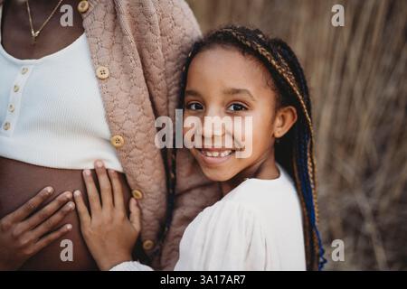 Mère enceinte noire et filles de race mixte touchant le ventre Banque D'Images