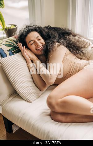 Femme souriante reposant sur un canapé avec un oreiller confortable Banque D'Images