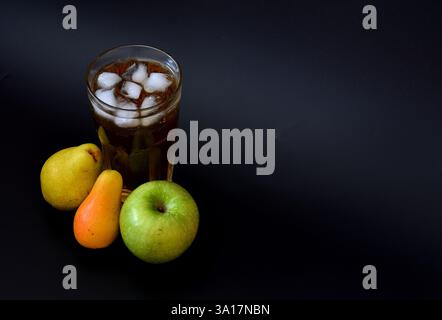 Mélange de jus de pomme et de poire dans un grand verre avec de la glace sur fond noir, fruits mûrs de différentes variétés à proximité. Gros plan. Banque D'Images