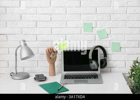 Lieu de travail moderne avec ordinateur portable, lampe, main en bois et papeterie près du mur blanc Banque D'Images