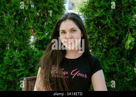 Jeune femme caucasienne souriante à l'extérieur avec fond de verdure. Banque D'Images