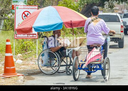 BANGKOK, THAÏLANDE, 13 APR 2024, Une femme sur un tricycle roule autour d'un vendeur de billets de loterie qui est assis dans un fauteuil roulant Banque D'Images