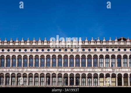 La façade ornée d'un bâtiment historique de la Piazza San Marco, présentant des fenêtres cintrées classiques et des détails architecturaux complexes. Banque D'Images