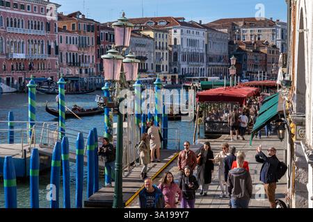Venise, Italie - 12 octobre 2024 : touristes marchant le long d'une promenade au bord de l'eau près du pont du Rialto avec des bâtiments historiques bordant le Grand canal. Banque D'Images