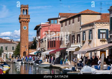 Venise, Italie - 12 octobre 2024 : la Torre dell’Orologio, une tour historique de l’horloge en briques rouges, s’élève au-dessus des paisibles canaux de Murano, reflétant le i. Banque D'Images