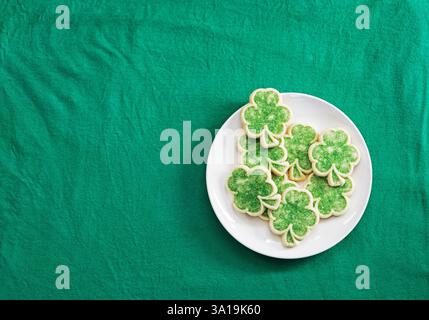 biscuits au sucre shamrock sur plaque blanche sur tissu vert plat posé par le haut Banque D'Images