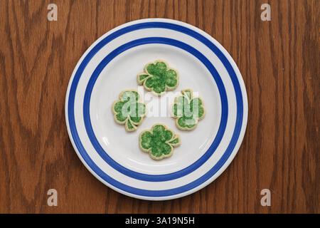 image du haut vers le bas de quatre biscuits au sucre de trèfle vert sur une plaque blanche avec des rayures bleues sur le bois Banque D'Images
