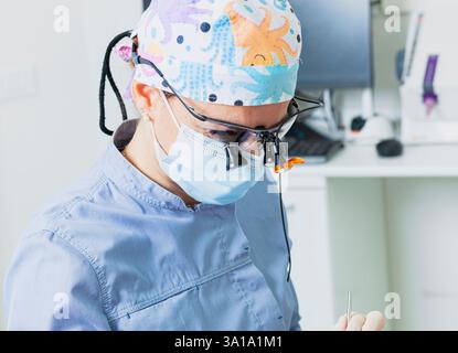 Dentiste femme portant des loupes chirurgicales et tenant des outils dentaires tout en effectuant un bilan dans sa clinique lumineuse Banque D'Images
