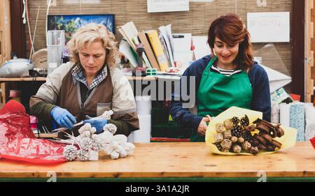 Deux fleuristes travaillent dans une pépinière. Couple travaille dans l'entreprise de jardinage sur une journée de travail ordinaire. Sur la photo une femme blonde et une jeune femme aux cheveux roux. Images authentiques. Banque D'Images