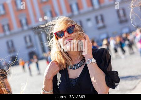 Belle femme aux cheveux blonds et aux lunettes rouge parle au téléphone. Banque D'Images