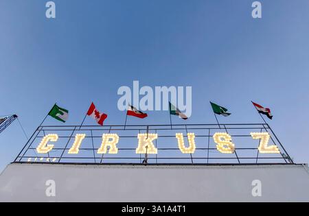 Panneau Cirkusz avec drapeaux internationaux illuminés et agitant au vent, face à un ciel bleu éclatant Banque D'Images
