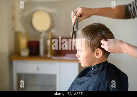 Le coiffeur amincit les cheveux du garçon avec des ciseaux amincissants. Banque D'Images
