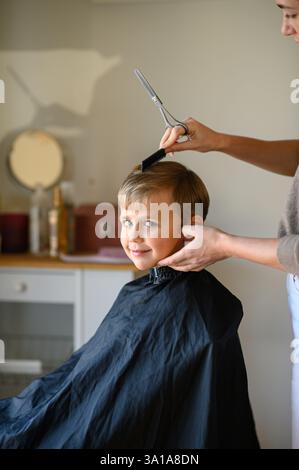 Le coiffeur amincit les cheveux du garçon avec des ciseaux amincissants. Banque D'Images