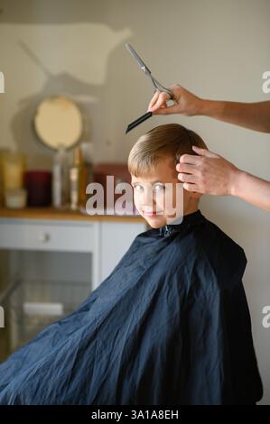 Le coiffeur amincit les cheveux du garçon avec des ciseaux amincissants. Banque D'Images