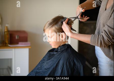 Le coiffeur amincit les cheveux du garçon avec des ciseaux amincissants. Banque D'Images
