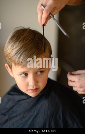 Le coiffeur amincit les cheveux du garçon avec des ciseaux amincissants. Banque D'Images