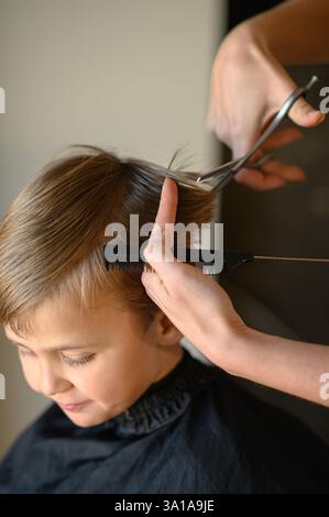 Le coiffeur amincit les cheveux du garçon avec des ciseaux amincissants. Banque D'Images
