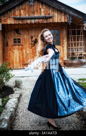 Femme dansant joyeusement dans un dirndl devant une cabane alpine Banque D'Images