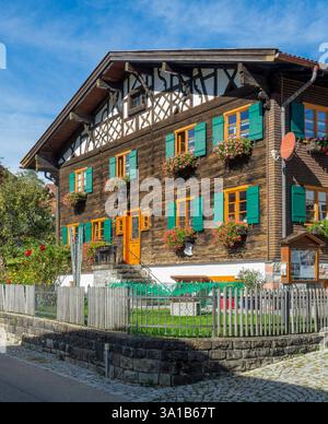 Rettenberg, Gästehaus Stork, vieille maison en bois avec pignon à colombages, fleurs devant les fenêtres et volets verts. Banque D'Images