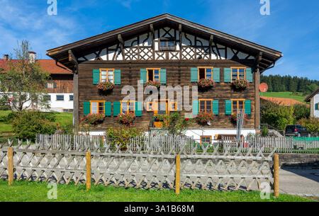 Rettenberg, Gästehaus Stork, vieille maison en bois avec pignon à colombages, fleurs devant les fenêtres et volets verts. Banque D'Images