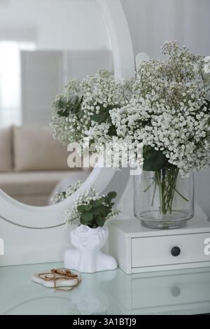 Bouquet de belles fleurs de gypsophila et branches d'eucalyptus dans un vase sur une coiffeuse près du miroir à l'intérieur Banque D'Images