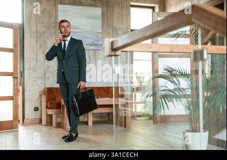 Bel homme en costume et cravate est debout à l'intérieur et tenant l'étui à la main. Banque D'Images