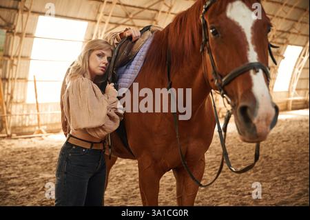 Prendre soin de l'animal. Belle jeune femme est avec cheval à l'intérieur. Banque D'Images
