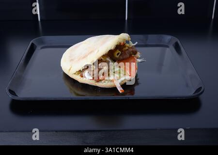 Un sandwich aux boulettes de viande est sur une assiette noire. Le sandwich est fait avec de la viande et des légumes Banque D'Images