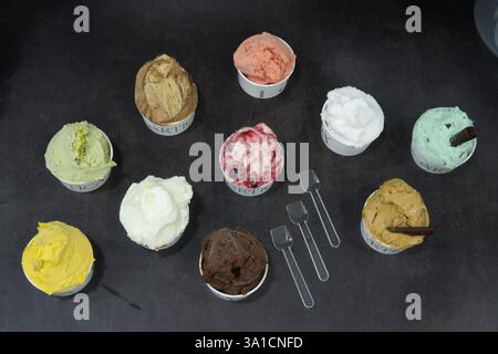Une rangée de tasses de crème glacée avec différentes saveurs, y compris le chocolat, la fraise et la vanille. Les tasses sont disposées en une rangée nette sur une table Banque D'Images