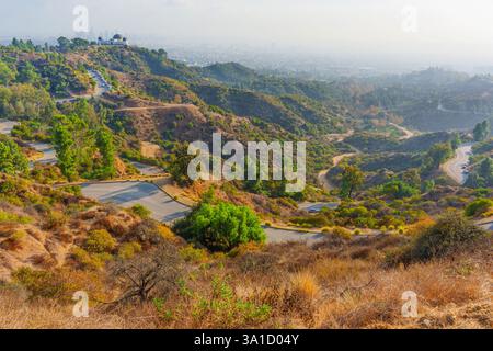 Vue imprenable sur les routes sinueuses menant à l'observatoire Griffith avec des collines et un horizon de Los Angeles brumeux en arrière-plan. Banque D'Images