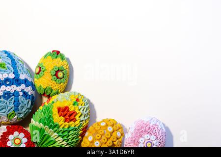Fond blanc de Pâques avec des œufs de Pâques colorés avec des ornements floraux et des décorations en origami dans le coin, espace de copie. Banque D'Images