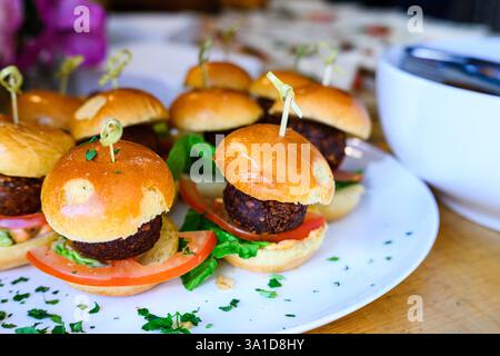Succulents mini-cheeseburgers servis sur une assiette magnifiquement garnie de tranches de laitue et de tomate, idéaux pour les fêtes, les hors-d'œuvre ou les amuse-gueules. Banque D'Images