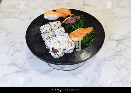 Une assiette de sushi avec une variété de différents types de sushi dessus. L'assiette est sur un comptoir en marbre Banque D'Images