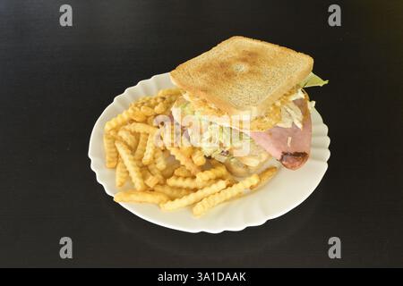 Un sandwich et des frites sur une assiette blanche. Le sandwich est grillé et contient de la laitue et du jambon Banque D'Images