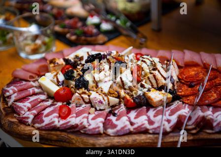 Un panneau de charcuterie coloré présente une gamme de charcuteries, fromages crémeux, olives et tomates cerises, magnifiquement agencés pour des rassemblements sociaux Banque D'Images