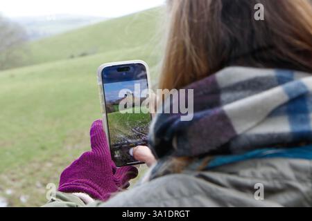 Femme prenant une photo de paysage avec smartphone dans la campagne portant des gants et une écharpe par temps froid. Colmers Hill, domaine Symondsbury ouest dorset uk Banque D'Images