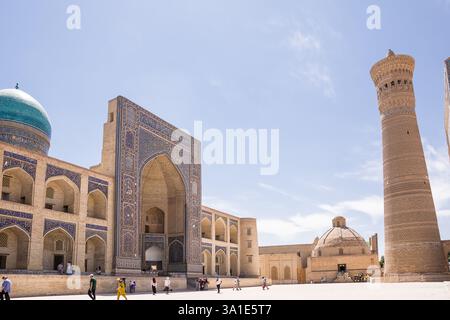 Boukhara, Ouzbékistan - 09 juillet 2024 : vue de la façade de la Madrassa, le minaret et la place avec des touristes à Boukhara Banque D'Images