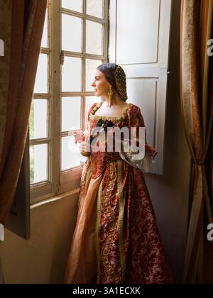 Femme portant un authentique costome de la Renaissance et une adresse debout à sa fenêtre dans un château médiéval Banque D'Images