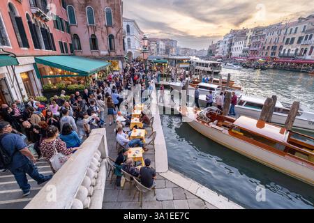 Venise, Italie - 12 octobre 2024 : vue depuis le pont du Rialto surplombant le Grand canal au coucher du soleil, avec des foules dans les cafés du front de mer et des bateaux naviguant sur le Banque D'Images