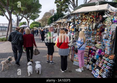 Venise, Italie - 12 octobre 2024 : les touristes parcourent un stand de souvenirs vendant des masques vénitiens, des porte-clés et d'autres souvenirs Banque D'Images