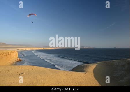 Parapente survolant l'océan Pacifique dans la réserve nationale de Paracas au coucher du soleil. ICA, Pérou Banque D'Images