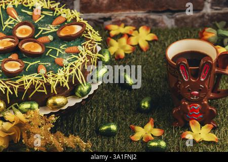 Un gâteau de Pâques à côté du lapin de Pâques, tasse à café et arrangement de fleurs sur l'herbe Banque D'Images