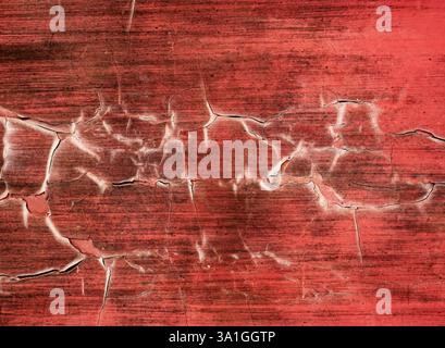 Gros plan détaillé de peinture rouge fissurée révélant des textures sur une vieille surface dans un environnement altéré Banque D'Images
