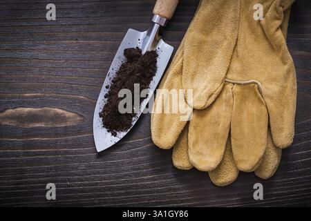 Bêche à main avec des gants de sécurité en terre et en cuir sur fond de bois vintage concept de jardinage Banque D'Images
