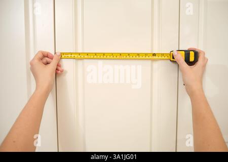 Mains d'une femme mesurant une armoire de cuisine avec un ruban à mesurer jaune. Concept d'amélioration de la maison et de rénovation. Banque D'Images