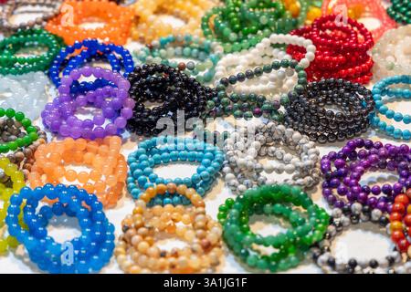 Bracelets de perles multicolores en verre poli et pierres semi-précieuses affichés sur un stand de marché réfléchissant la lumière et présentant une variété de Banque D'Images