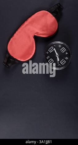 Masque de sommeil rouge et réveil isolé sur fond gris foncé. Concept de journée mondiale du sommeil Banque D'Images
