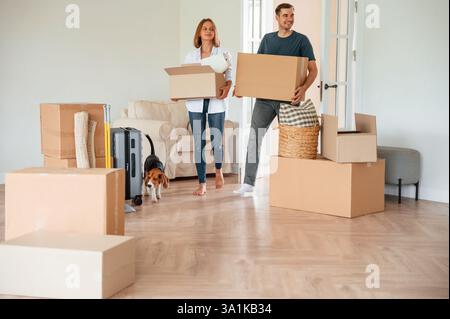 Les nouveaux propriétaires sourient. Jeune couple avec chien déménagent à la nouvelle maison. Banque D'Images