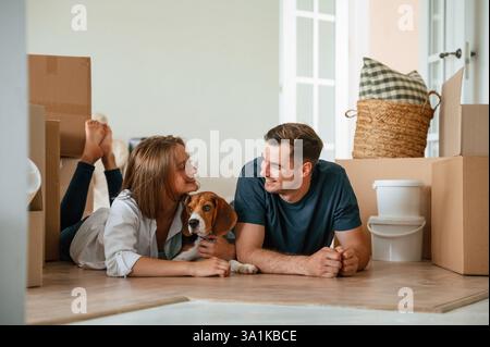 Les nouveaux propriétaires sourient. Jeune couple avec chien déménagent à la nouvelle maison. Banque D'Images